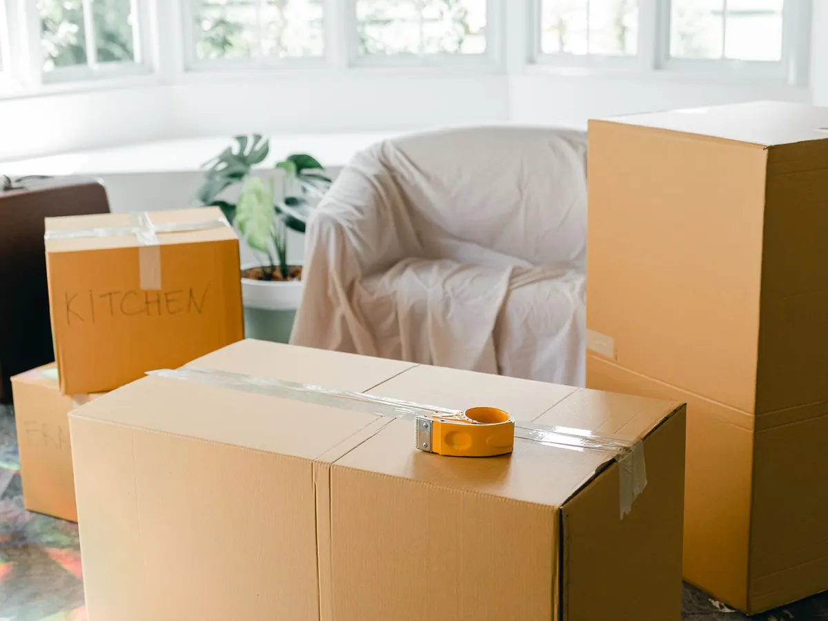 Verpackte Umzugskartons und ein abgedeckter Sessel in einer hellen, fast leeren Wohnung